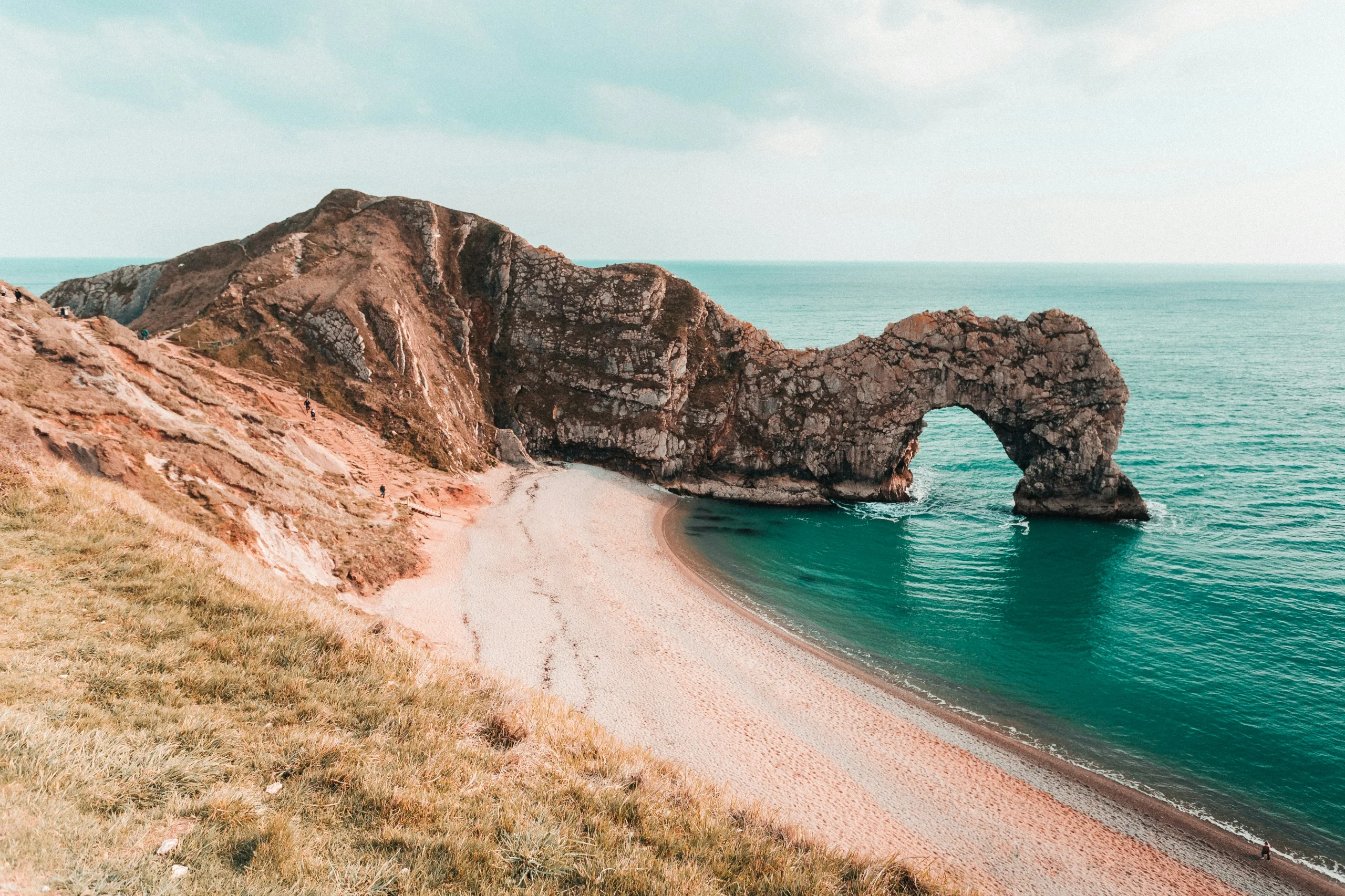 Durdle Door, the natural limestone arch on Dorset's Jurassic Coast, with the beach and clear blue sea below