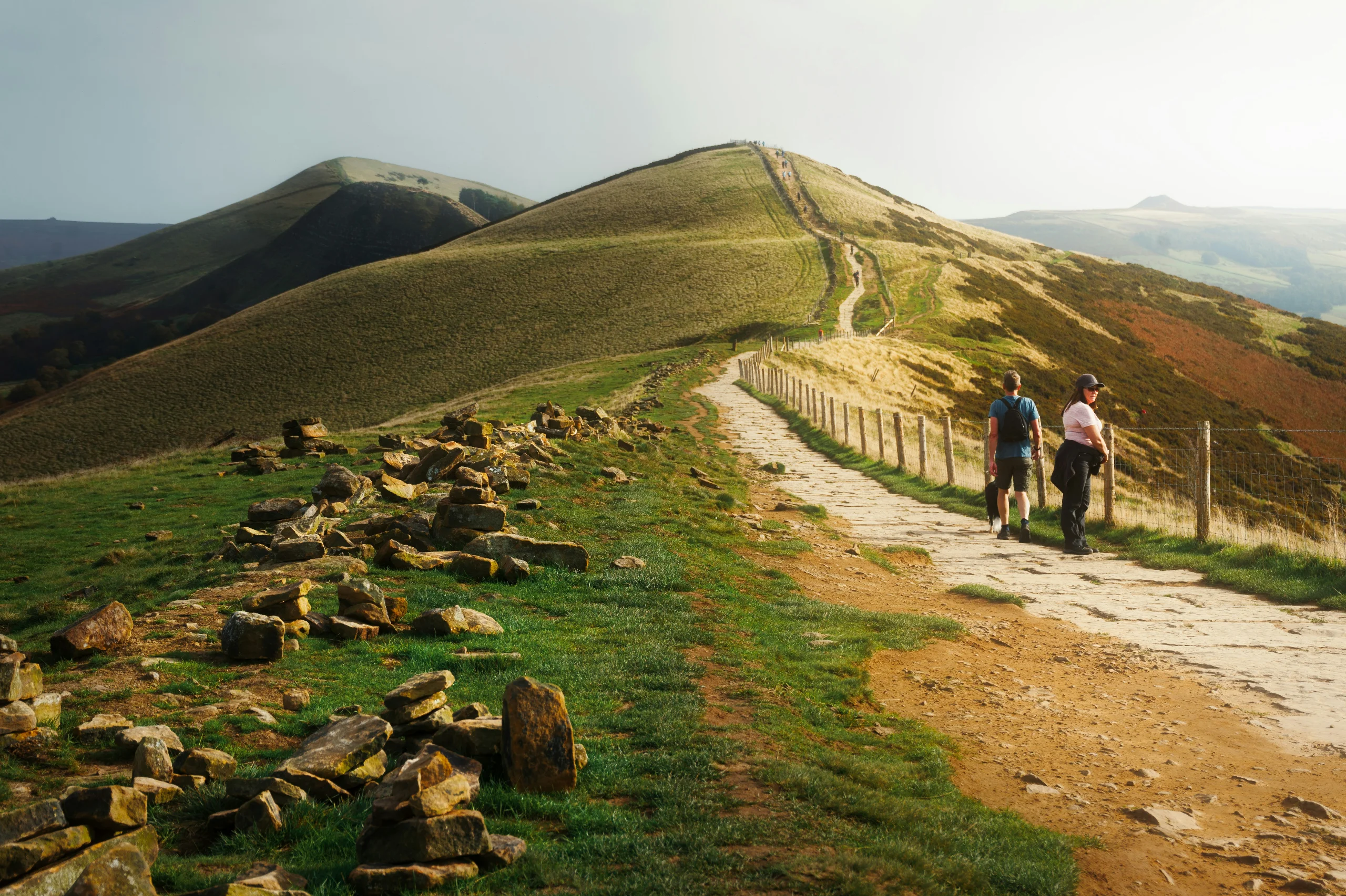 Walkers on the paved path along the ridge of Mam Tor in the Peak District, with the Hope Valley below