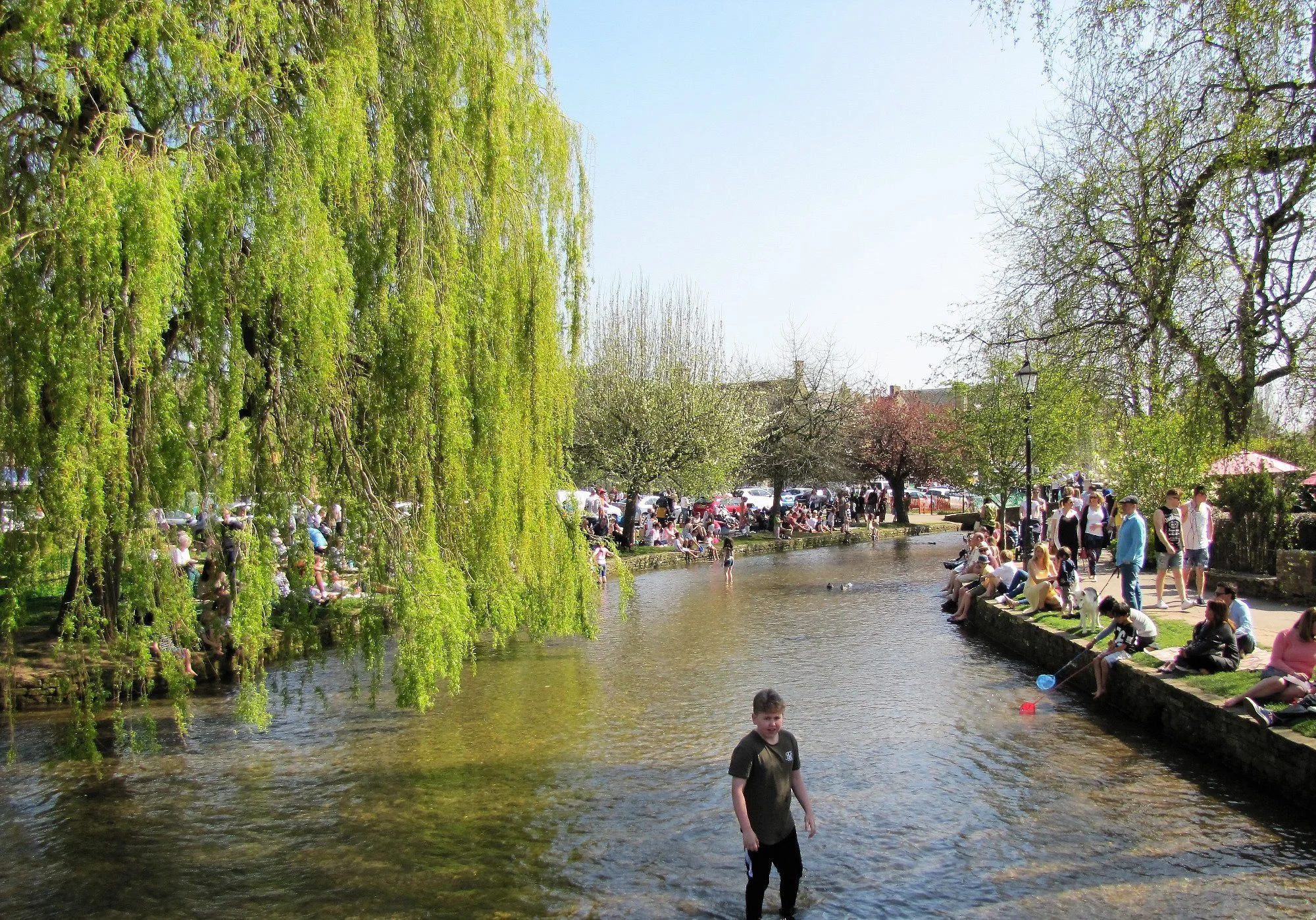 Children paddling in the shallow River Windrush beneath the low stone bridges of Bourton-on-the-Water in the Cotswolds