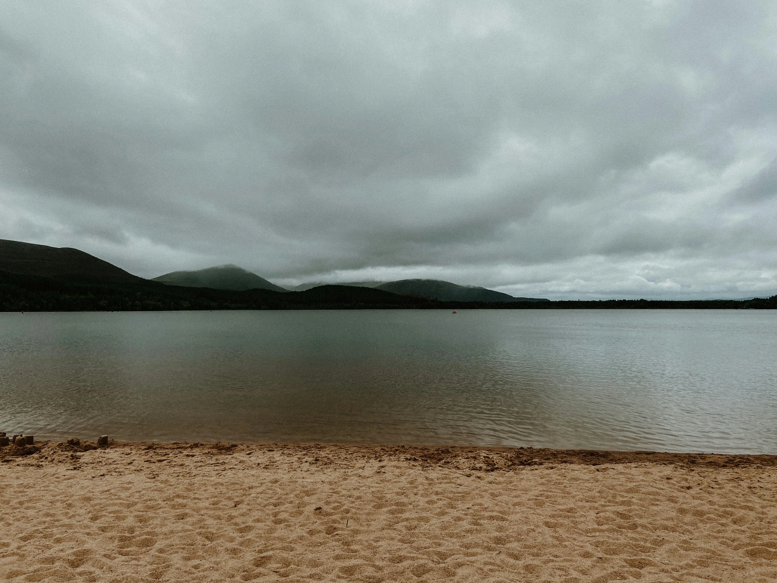The sandy beach at Loch Morlich near Aviemore, with pine forest and the Cairngorm mountains behind