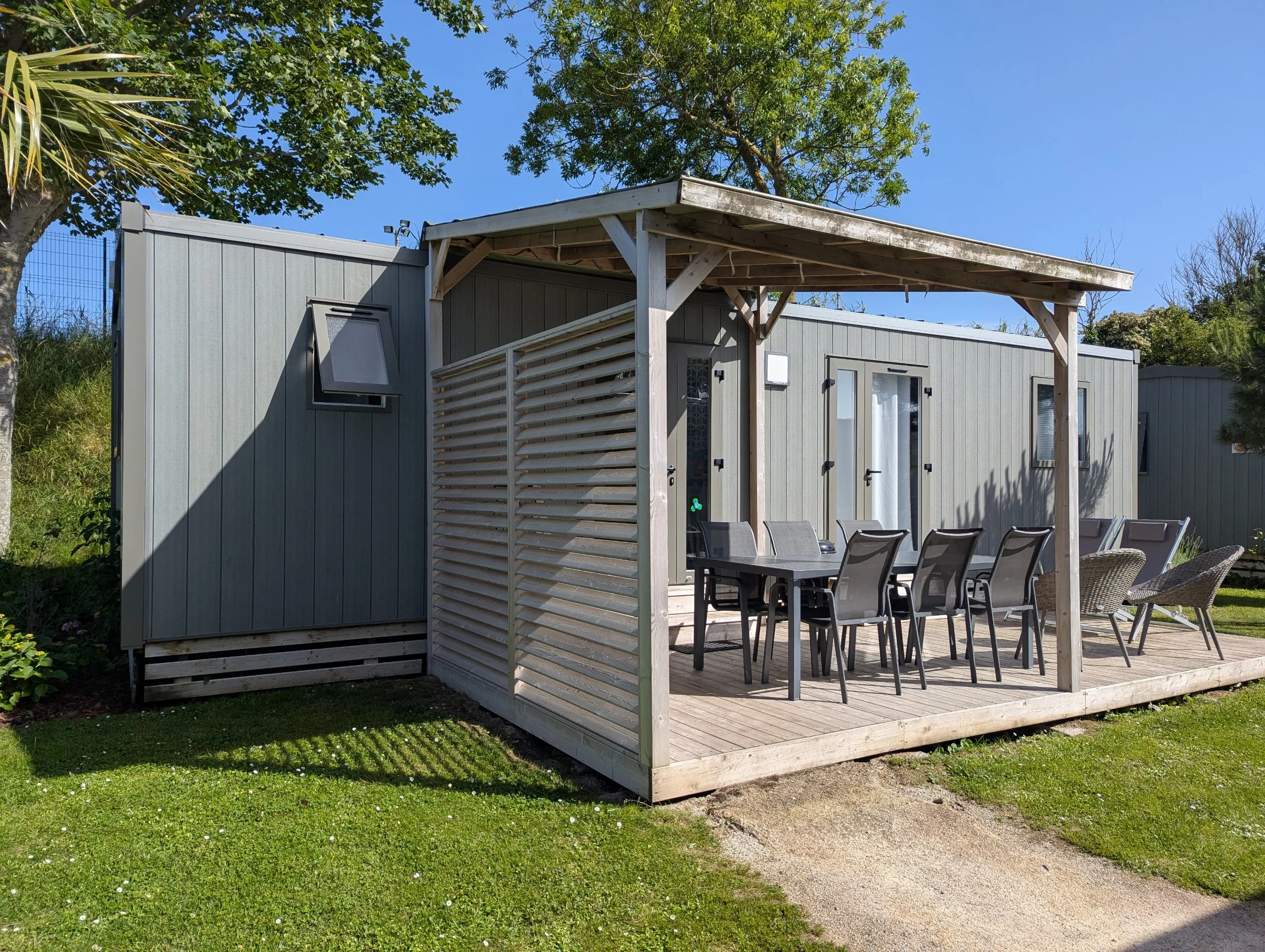 Large grey wooden camping cabin with a decking with tables and chairs