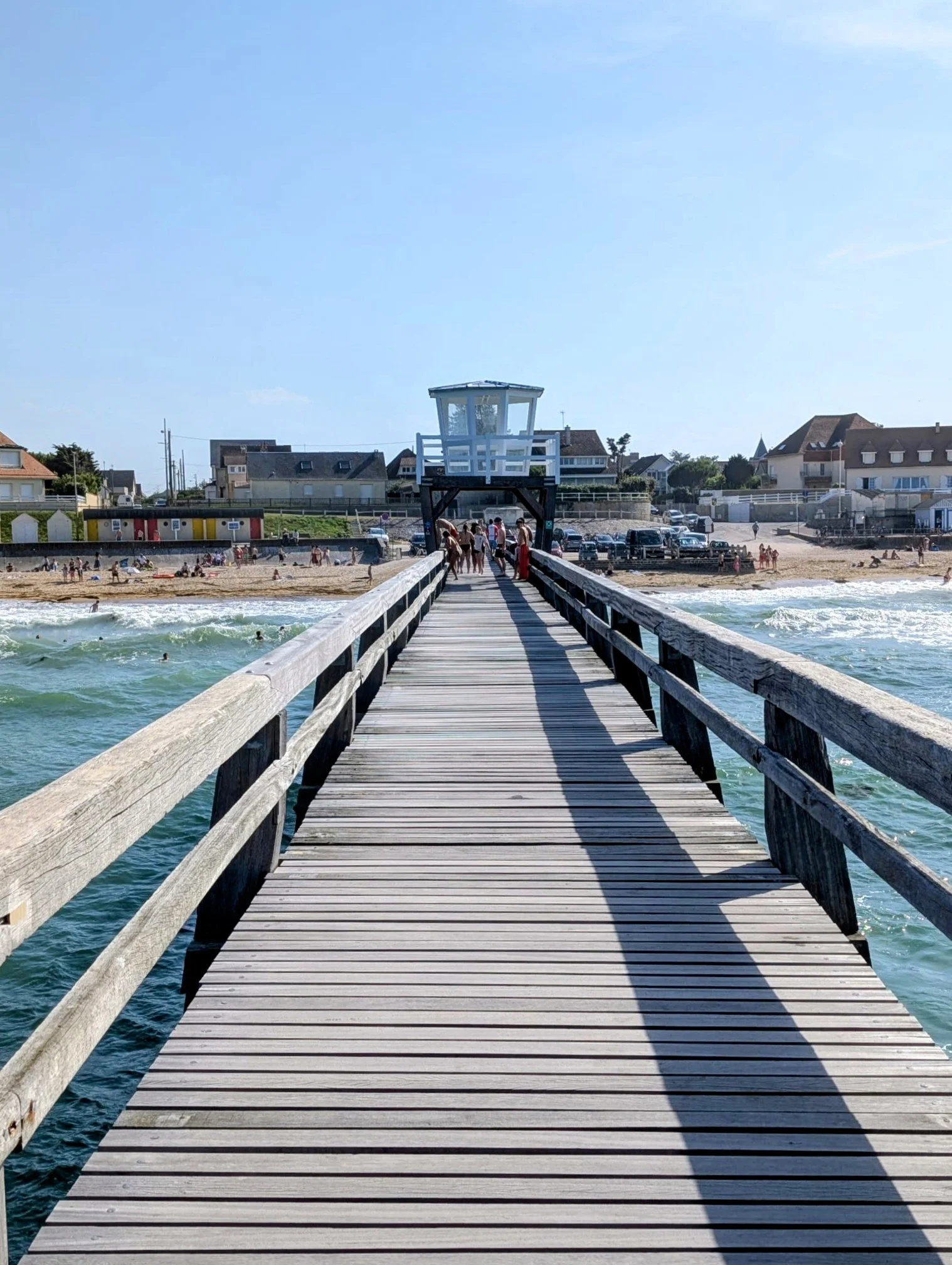 long wooden pier looking back to the shore with people jumping off into the sea