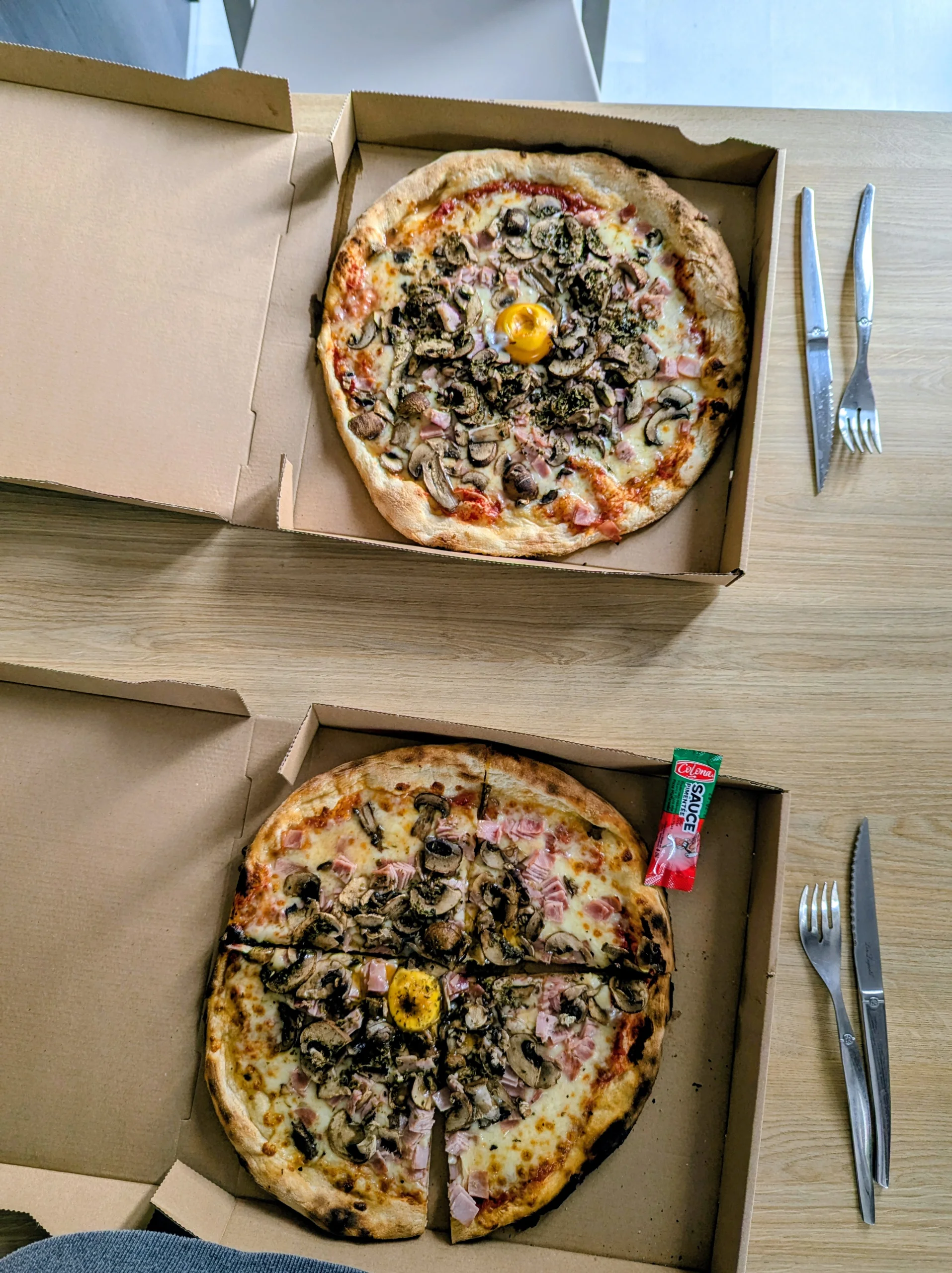 2 ham and mushroom pizzas in open takeout boxes on a table