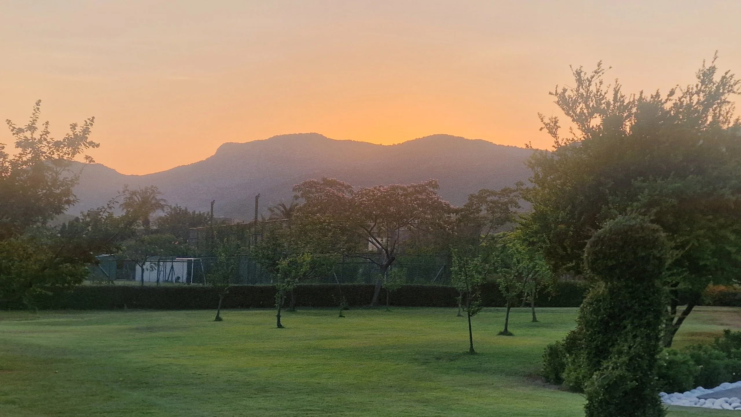 sun setting behind mountains behind a hotel garden