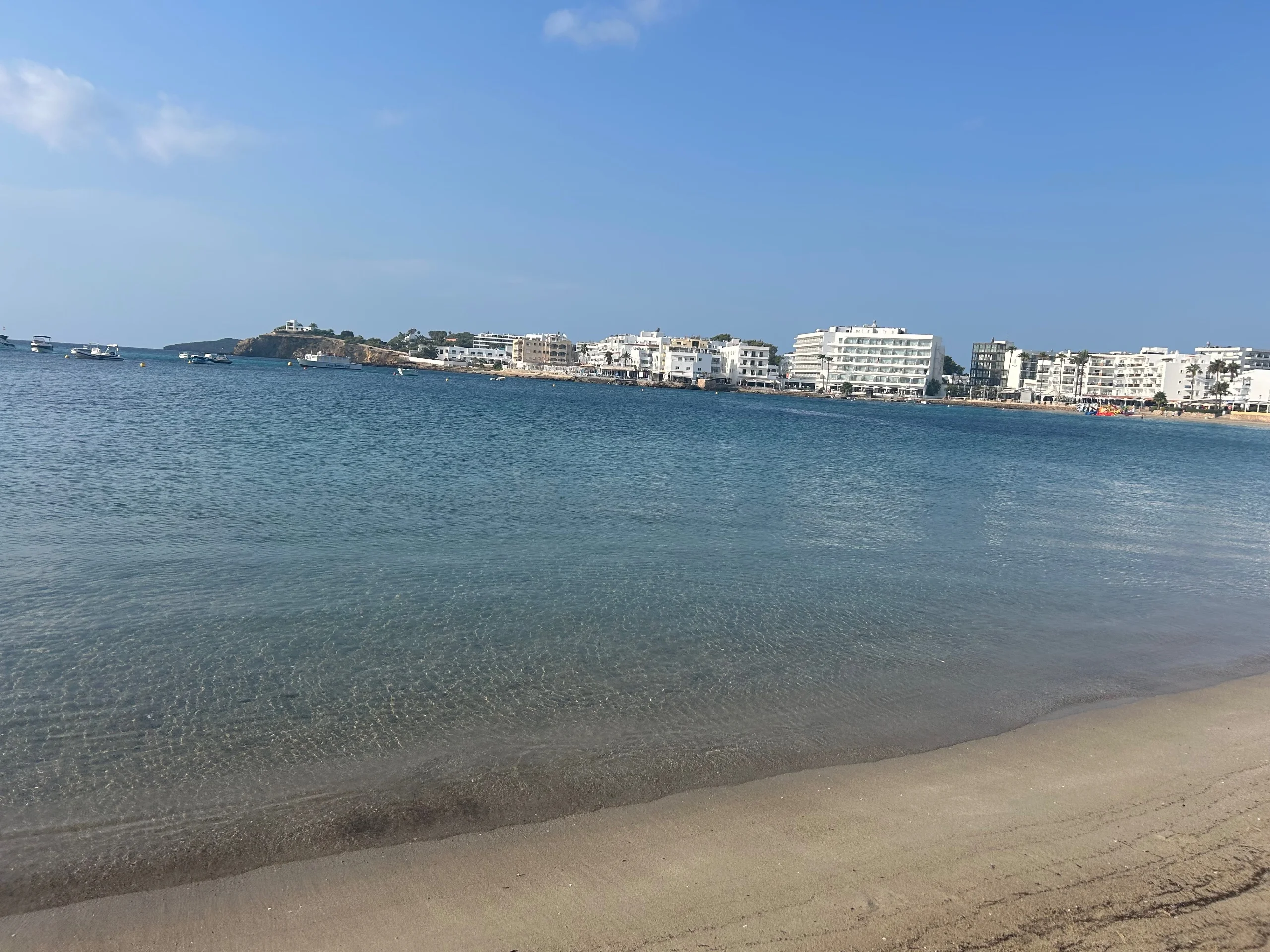 Shallow clear water at Es Canar beach with white hotels along the shoreline