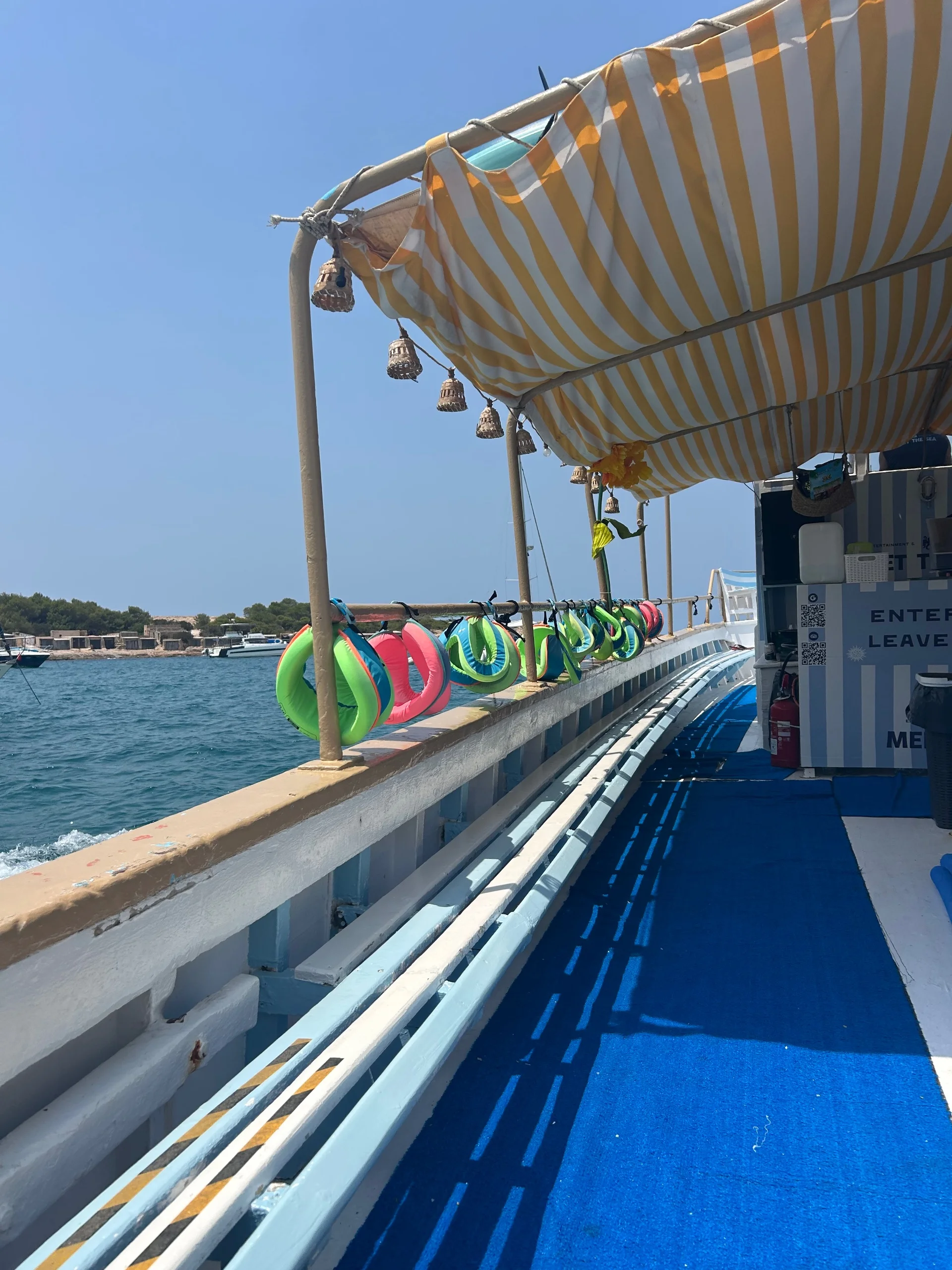 Inflatable rings hanging along the rail of the Meet The Sea boat under a yellow and white striped canopy